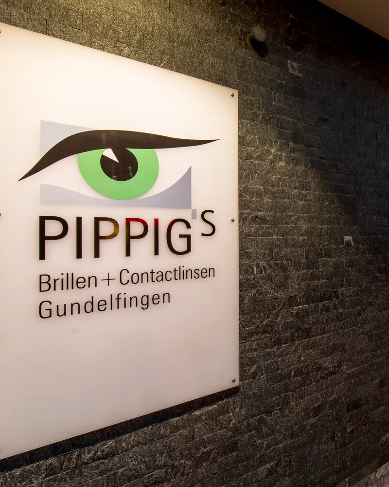 Das beleuchtete Firmenschild mit dem grünen Auge an der Außenwand